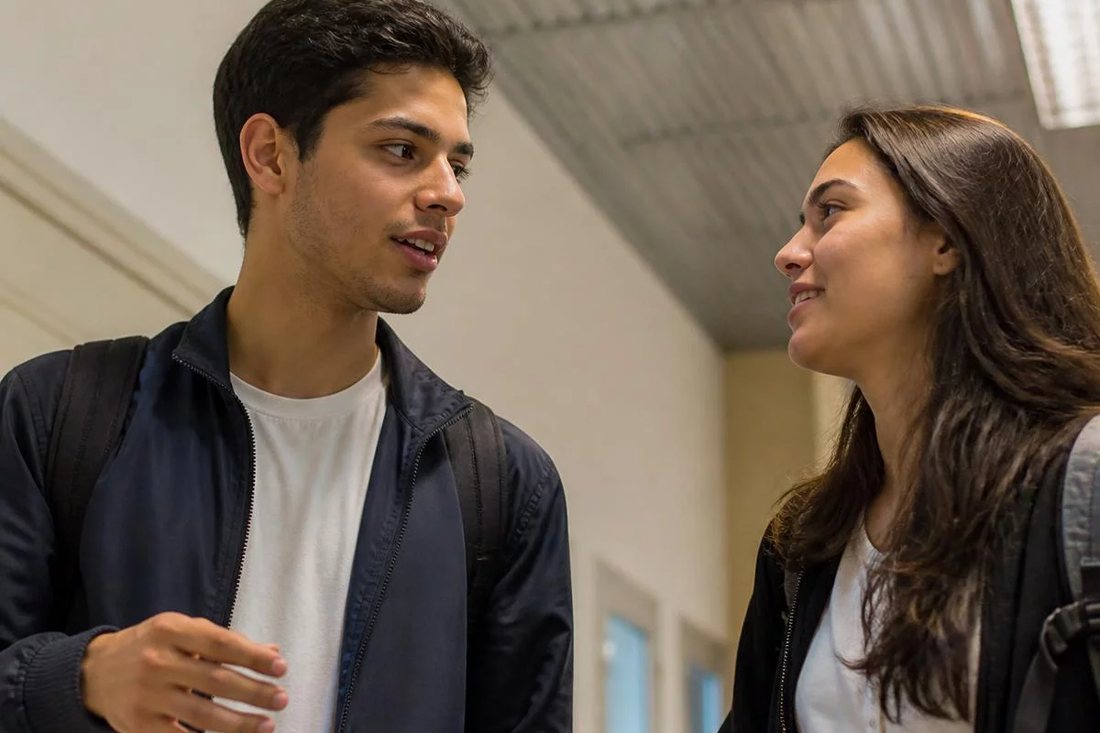 Dois estudantes de mochila continuam a discussão no corredor depois da sessão
